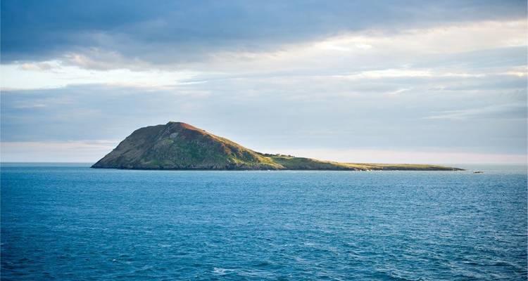 Kleine grasbewachsene Insel, die sich aus ruhigem blauem Meer unter sanftem Nachmittagslicht erhebt