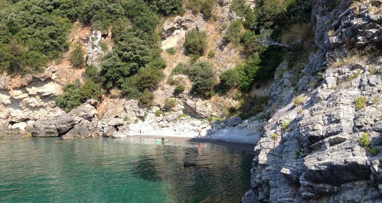 Abgelegener Kieselstrand mit smaragdgrünem Wasser, eingebettet unter Felsklippen und üppiger Vegetation.