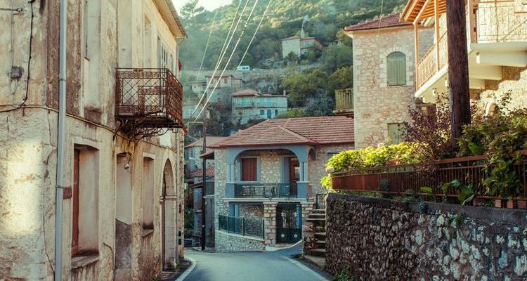 Une rue étroite dans un village avec des maisons en pierre et de la verdure.