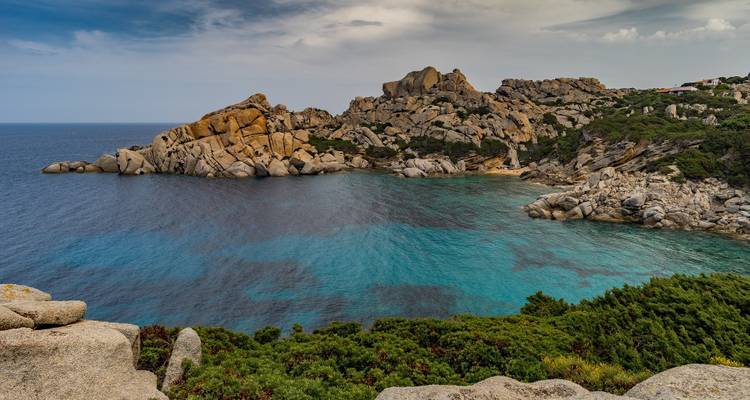 Une baie rocheuse isolée avec une eau bleue claire entourée de verdure.