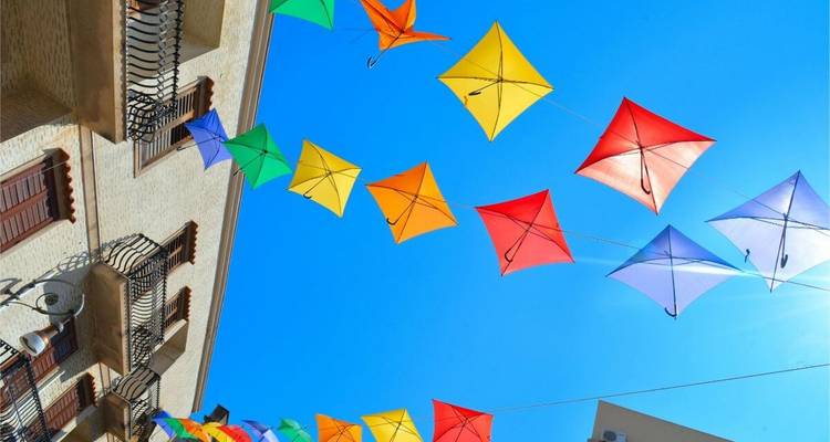 Bunte Drachen fliegen über Gebäuden unter einem hellen Himmel.