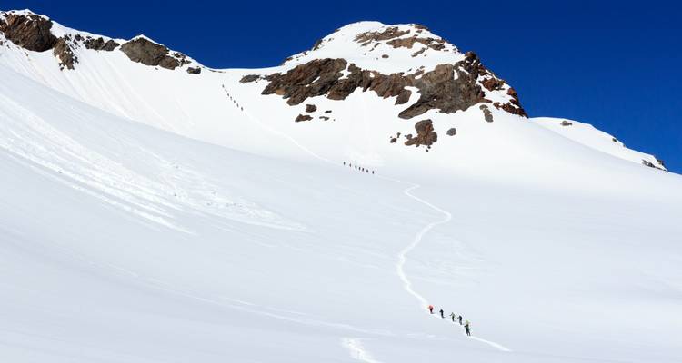 Een rij klimmers die een besneeuwde berghelling beklimmen.