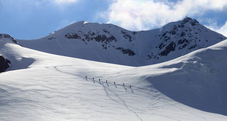 Groep skiërs die een besneeuwde omgeving doortrekt met bergtoppen op de achtergrond.