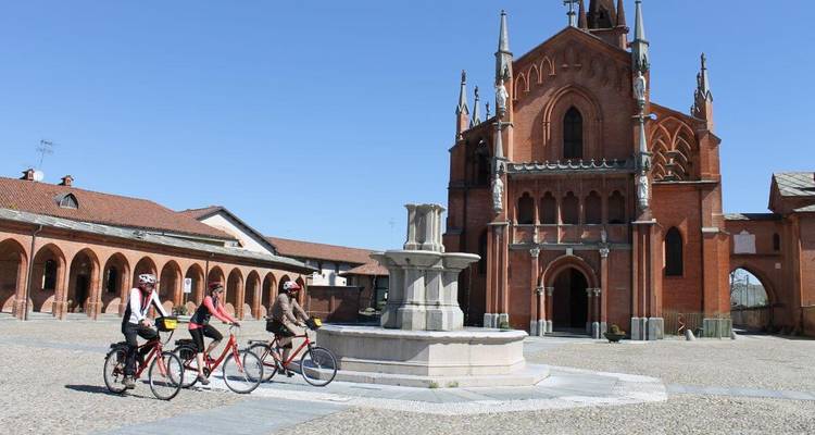 Cyclistes sur une place avec une vieille église et une fontaine.
