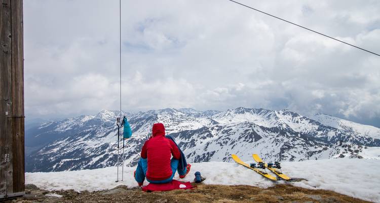 Une personne assise sur un sommet de montagne enneigé surplombant la chaîne.