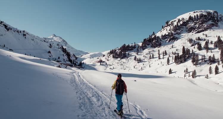 Un randonneur marchant sur un sentier enneigé dans les montagnes.