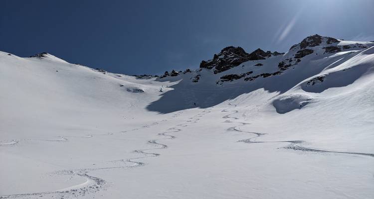Paysage de montagne enneigé avec des pistes de ski sous un ciel dégagé.