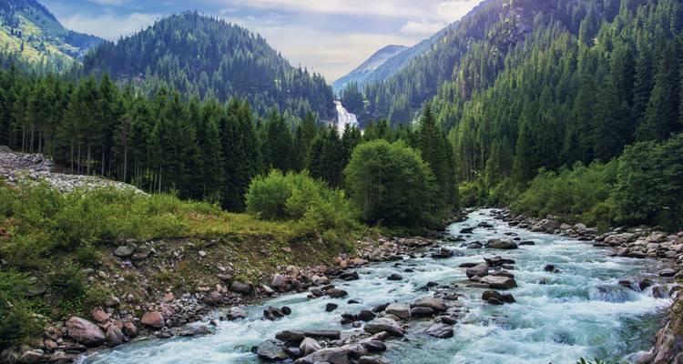 Fluss in einem Tal mit Bergen und einem Wasserfall in der Ferne.