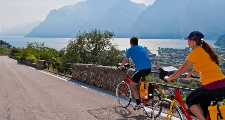 Zwei Radfahrer fahren ein Tandem entlang einer Seestraße mit Blick auf Berge und Wasser