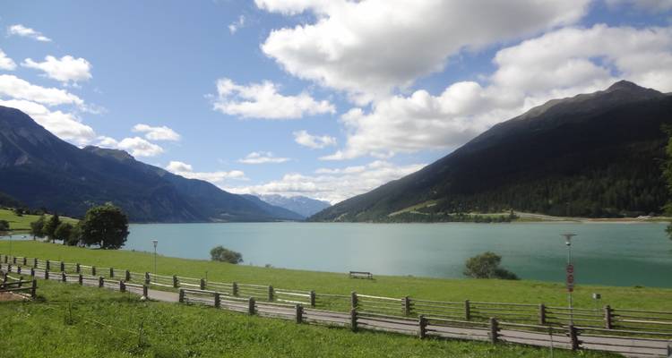 Calm lake surrounded by mountains and clouds.