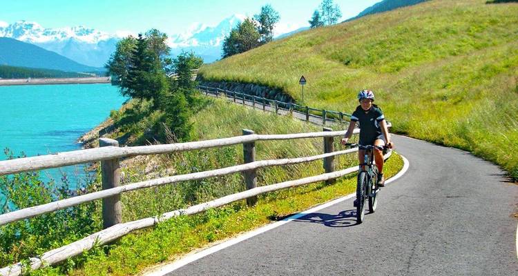 Cyclist on a scenic path by a turquoise lake.