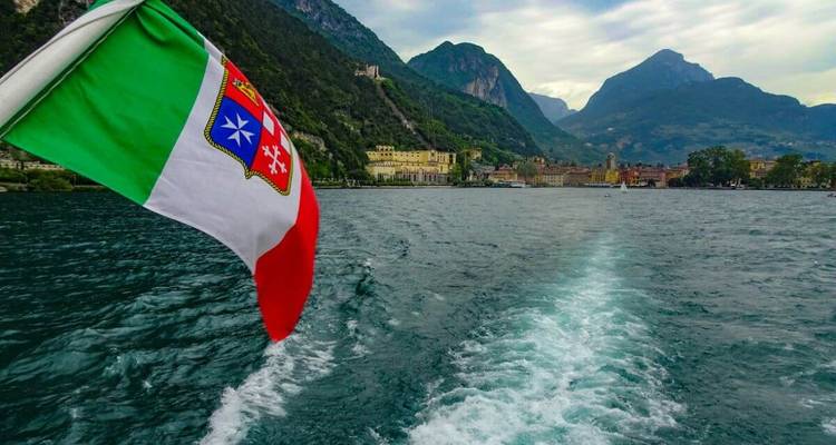 Drapeau italien sur un bateau avec un lac et des montagnes en arrière-plan.