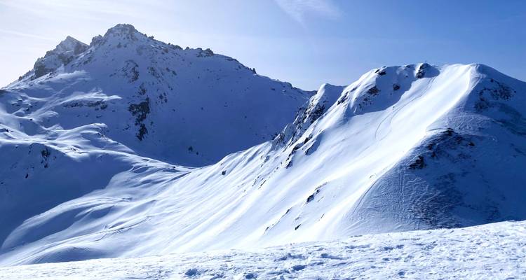 Pendientes y crestas de nieve blanca brillante bajo un cielo azul despejado en altas montañas.