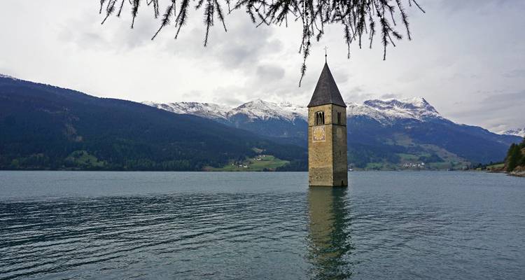 Submerged bell tower in a lake with mountains in the background.