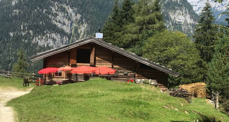 Chalet rustique dans un cadre montagnard avec des parasols rouges sur la pelouse.