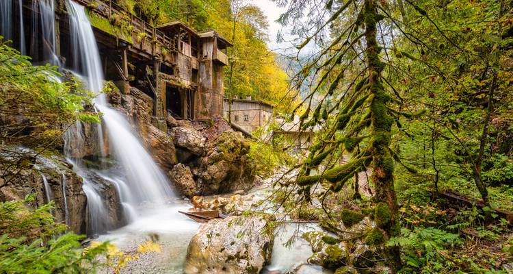 Waterval die naast rustieke gebouwen in een bos naar beneden stroomt.