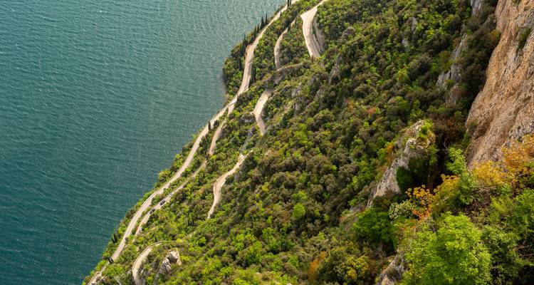 Route sinueuse le long d'une colline escarpée avec une végétation dense.