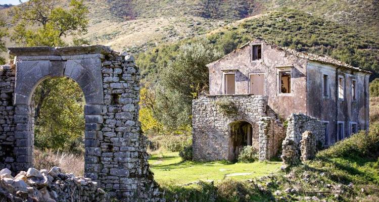 A historic stone house and arch ruins in a rural landscape.