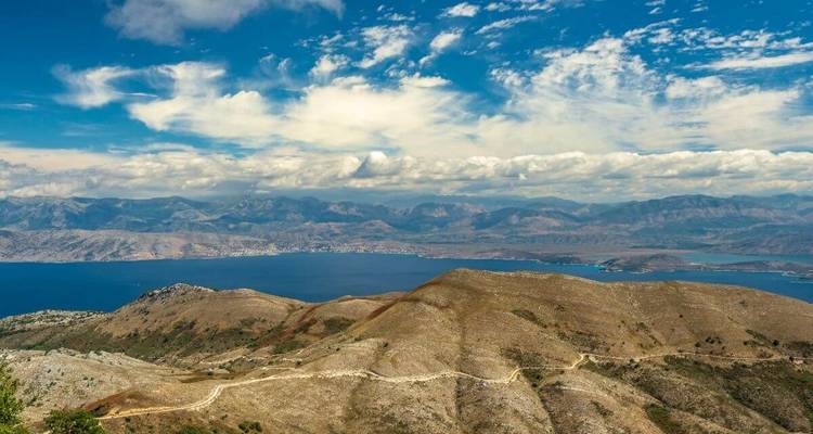 A scenic view of mountains and the sea under a blue sky with scattered clouds.