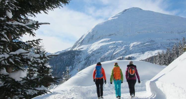 Trois randonneurs marchant sur un sentier enneigé avec un paysage montagneux en arrière-plan.