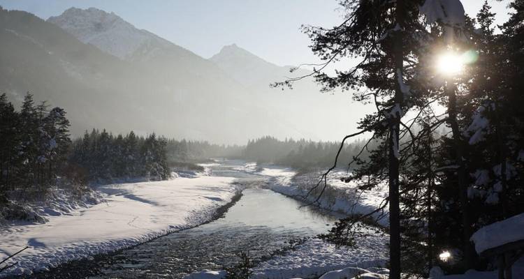 Paysage enneigé avec une rivière qui coule à travers et le soleil qui perce à travers les arbres.
