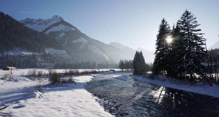 Rivière traversant une vallée enneigée sous un ciel lumineux.