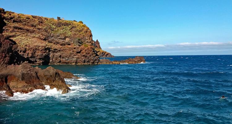 Promontorio rocoso volcánico que se eleva desde las aguas azul profundo del Atlántico bajo un cielo despejado en Madeira.
