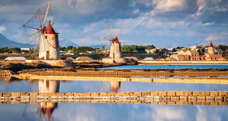 Traditionelle Windmühlen, die sich in Salzebenen unter einem dramatischen Himmel spiegeln.