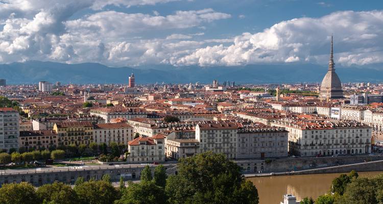 Stadtansicht mit markanter Turm und Bergen im Hintergrund.