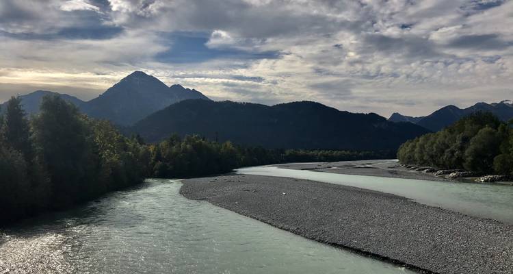 Paysage de montagne avec une rivière et des montagnes lointaines sous un ciel nuageux.