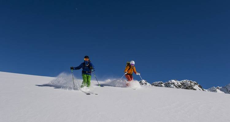 Deux skieurs descendant une pente enneigée sous un ciel dégagé.