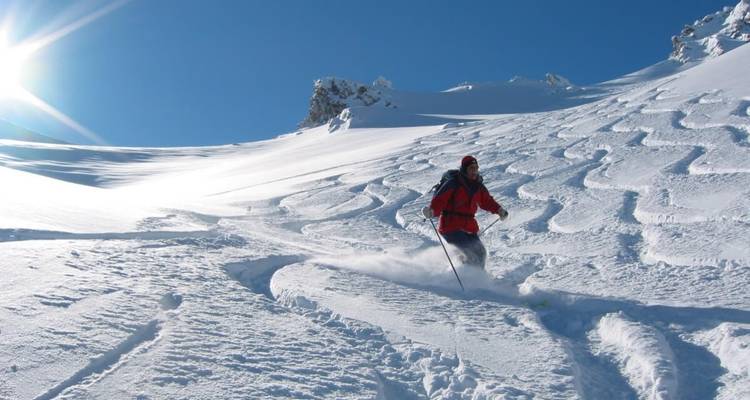 Un skieur effectuant des virages dans de la poudreuse fraîche par une journée ensoleillée.