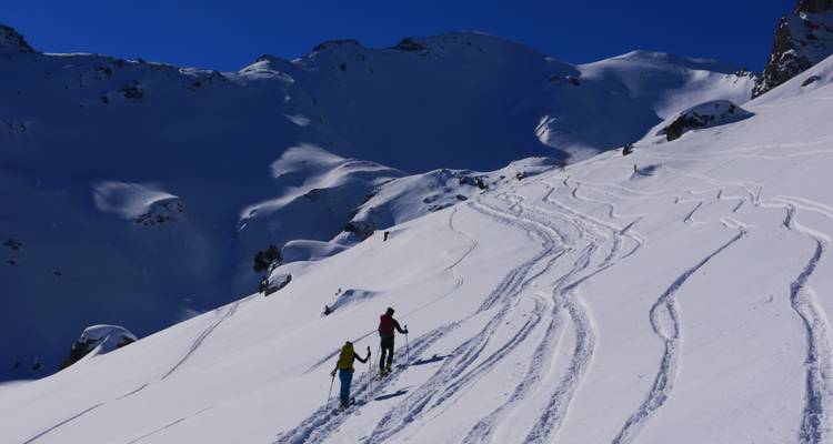 Deux personnes faisant de la randonnée sur une montagne couverte de neige, marquée de traces de ski.