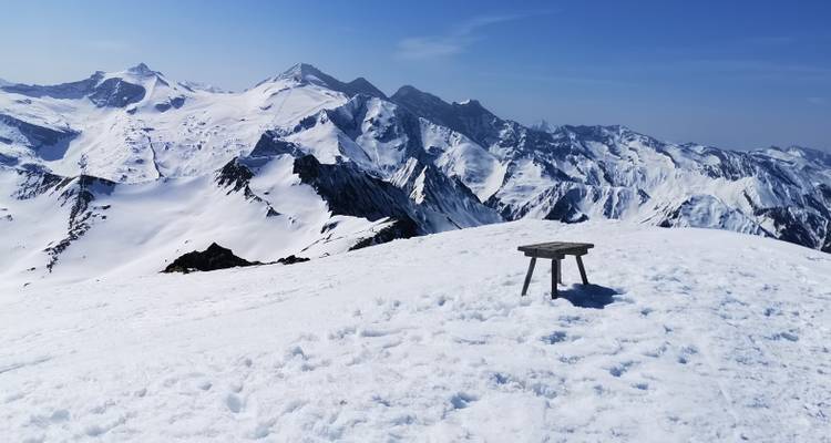 Un banc sur une crête de montagne enneigée surplombant de vastes sommets enneigés.