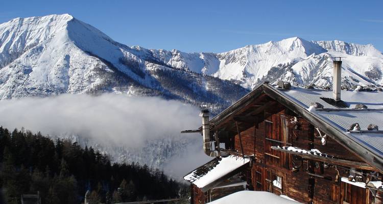Un chalet de montagne enneigé avec un ciel bleu clair et des sommets environnants.