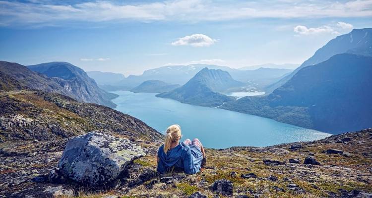 Person relaxing on a mountainside overlooking lakes and valleys.