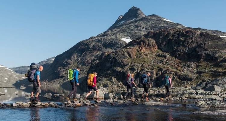 Hikers crossing a river in a rugged mountain landscape.