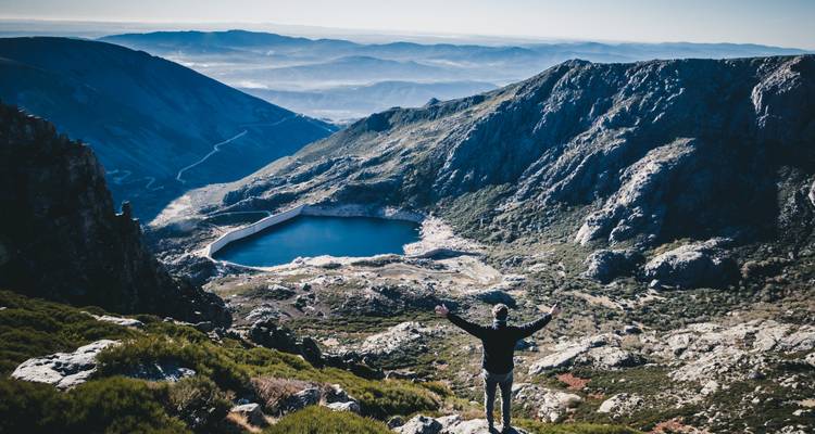 Personne avec les bras levés debout surplombant un lac de montagne.