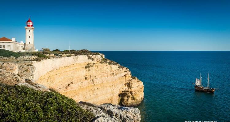 Vue de falaise d'un phare et d'un voilier sur la mer.