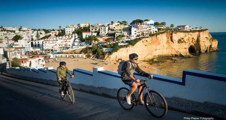 Deux personnes faisant du vélo près d'une plage et de falaises.