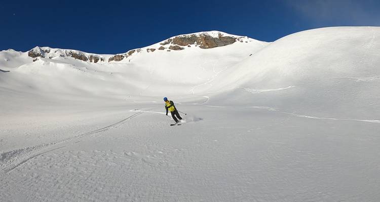 Personne skiant sur une large pente enneigée avec des montagnes au loin.