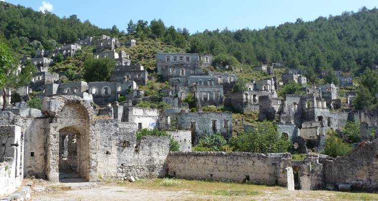 Ruined village with dilapidated stone buildings on a forested hill.