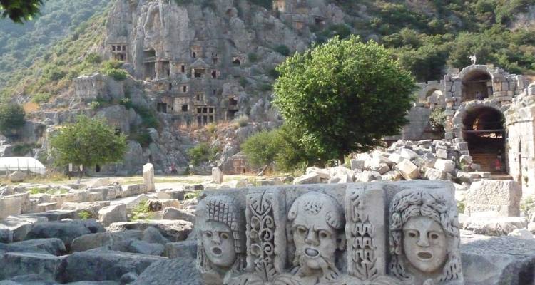 Ancient ruins with carved stone faces and cliffside tombs.