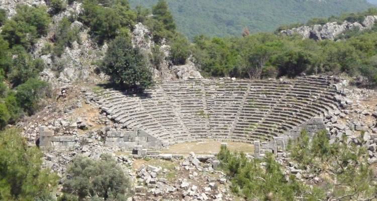 Ancient amphitheater surrounded by rugged hills and trees.