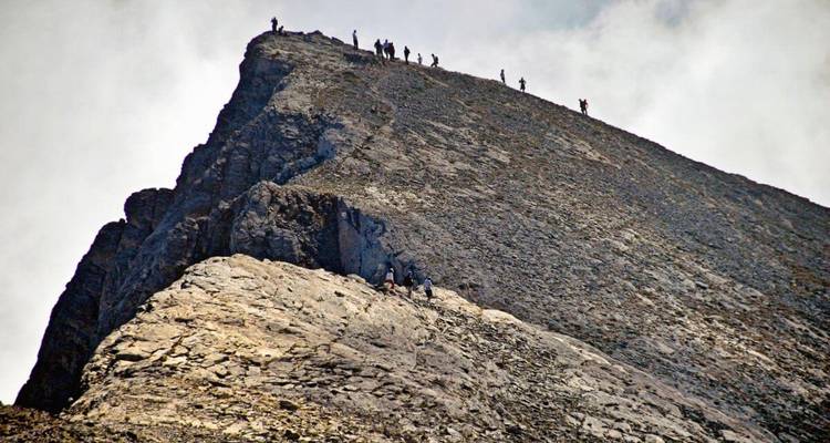 Hikers climbing a steep, rocky mountain peak.