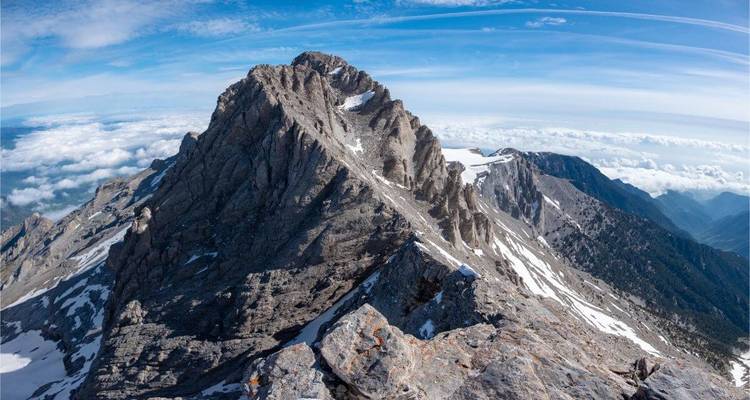 A dramatic mountain peak with snow patches and clouds.