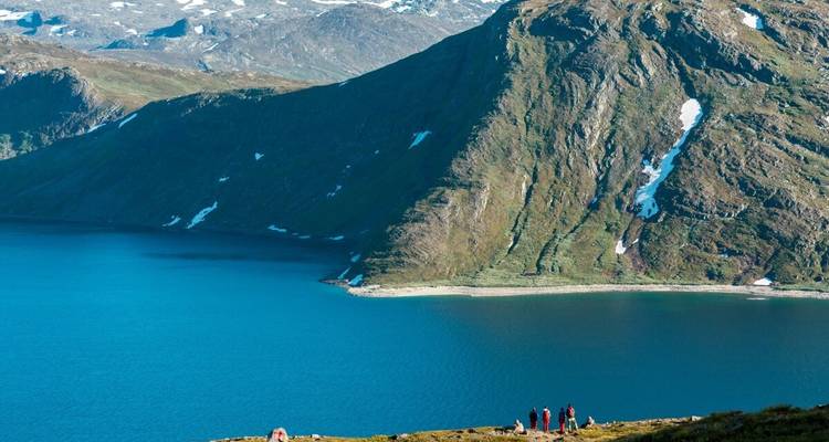 People hiking along the edge of a lake with mountainous views.