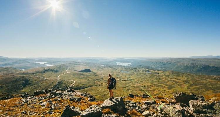 Hiker on a mountain top with vast valleys and lakes below.