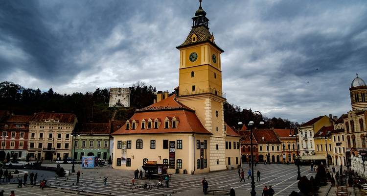 Place animée de Brasov avec sa tour d'horloge jaune et ses immeubles baroques colorés bourdonnant de foules.