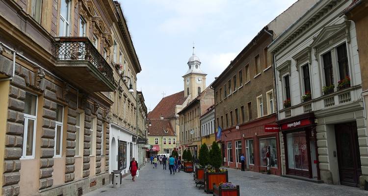Rue pavée de galets réservée aux piétons, bordée de façades historiques, de boutiques et de visiteurs se promenant dans la vieille ville de Brasov.